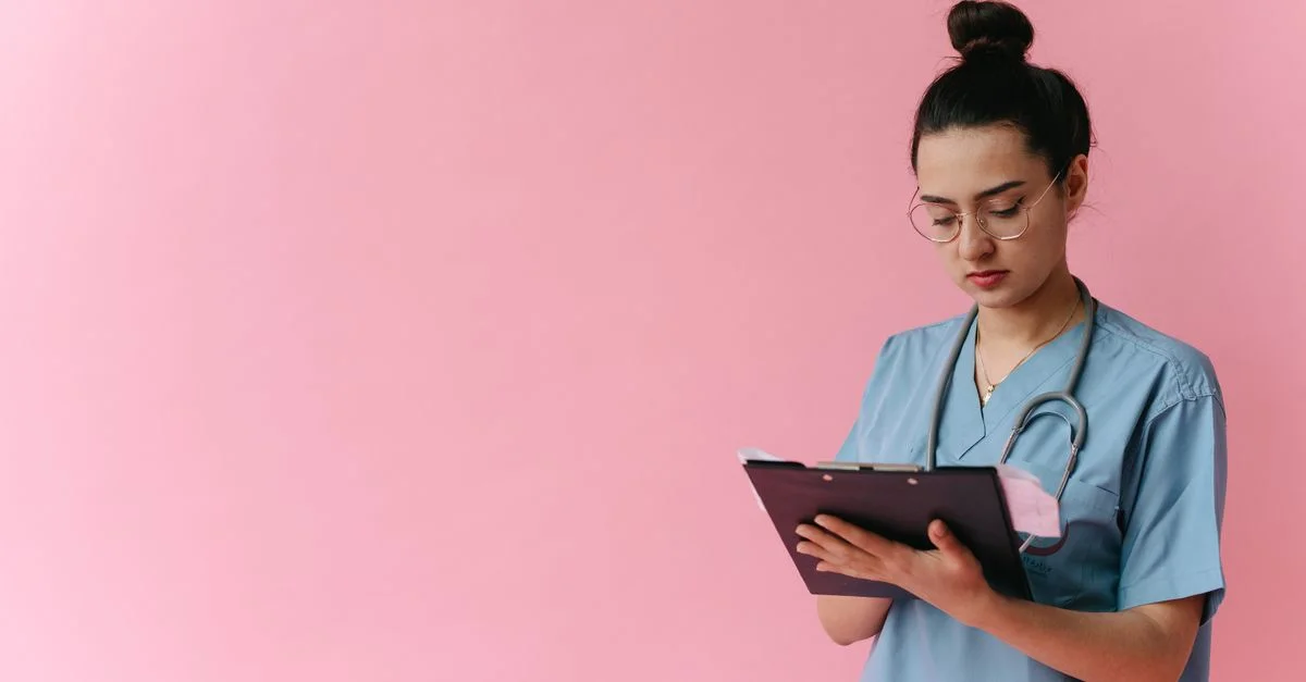Infirmière professionnelle examinant des notes de patients sur un clipboard avec un fond rose, dans un studio.
