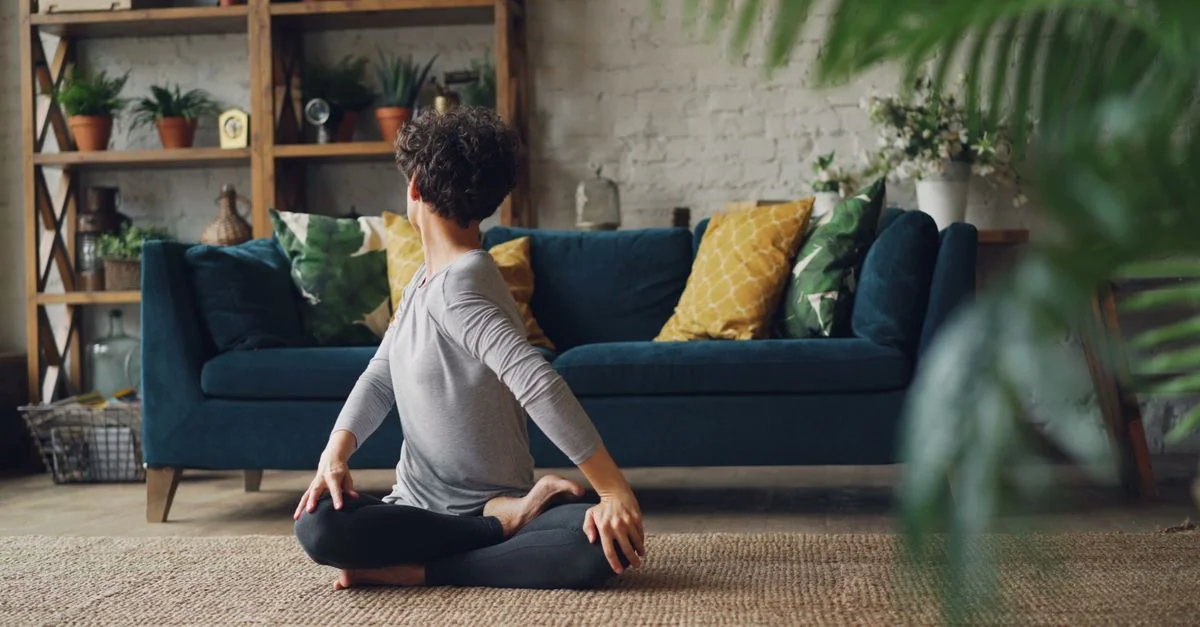 Femme pratiquant le yoga assis dans un salon intérieur confortable avec des plantes.