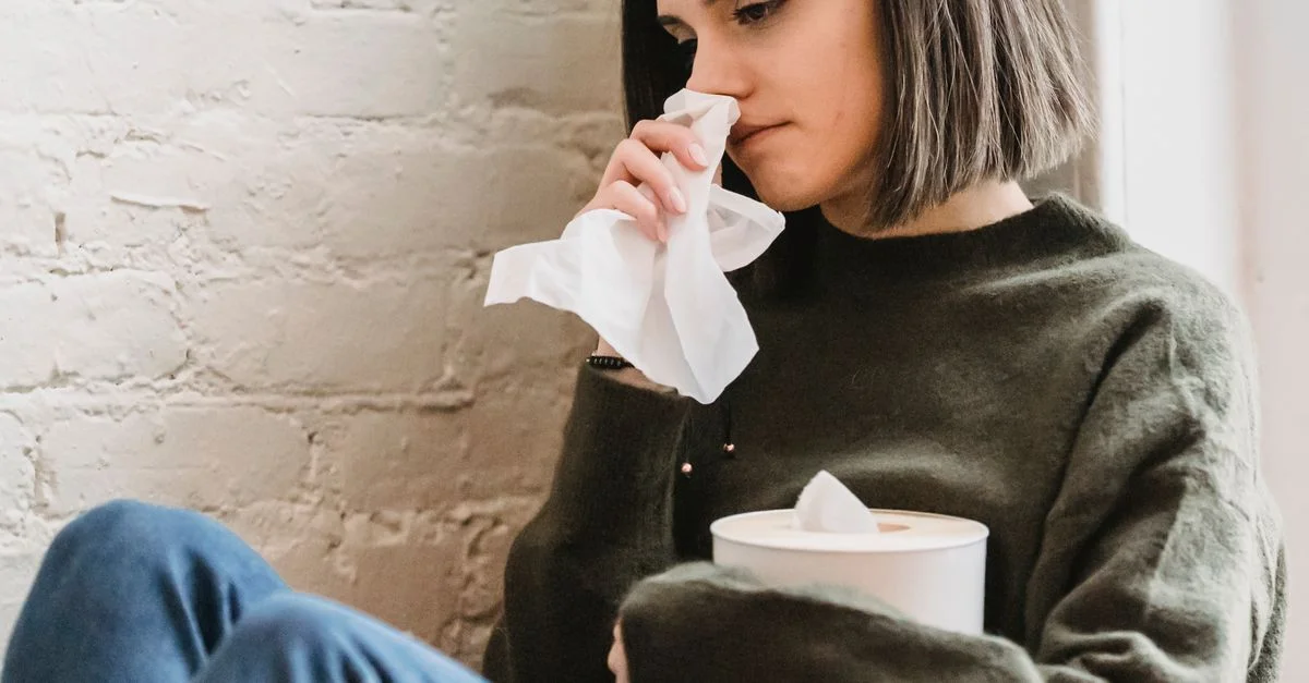 Jeune femme en vêtements décontractés assise à l'intérieur, tenant un mouchoir, illustrant la tristesse et la réflexion.