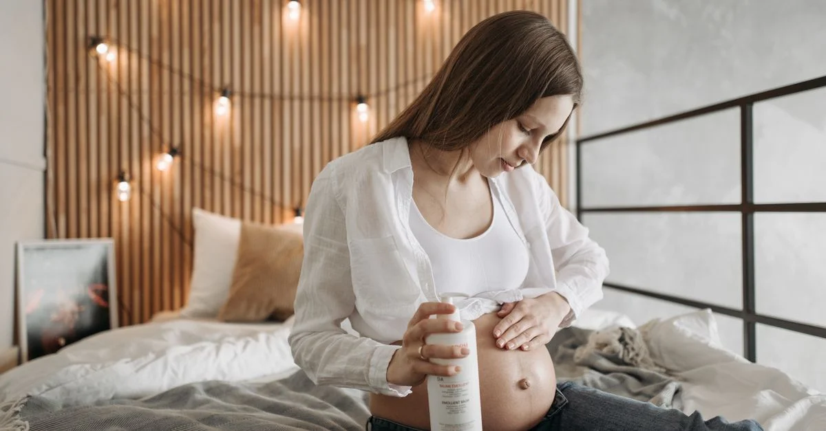 Femme enceinte assise à l'intérieur appliquant un hydratant sur son ventre.