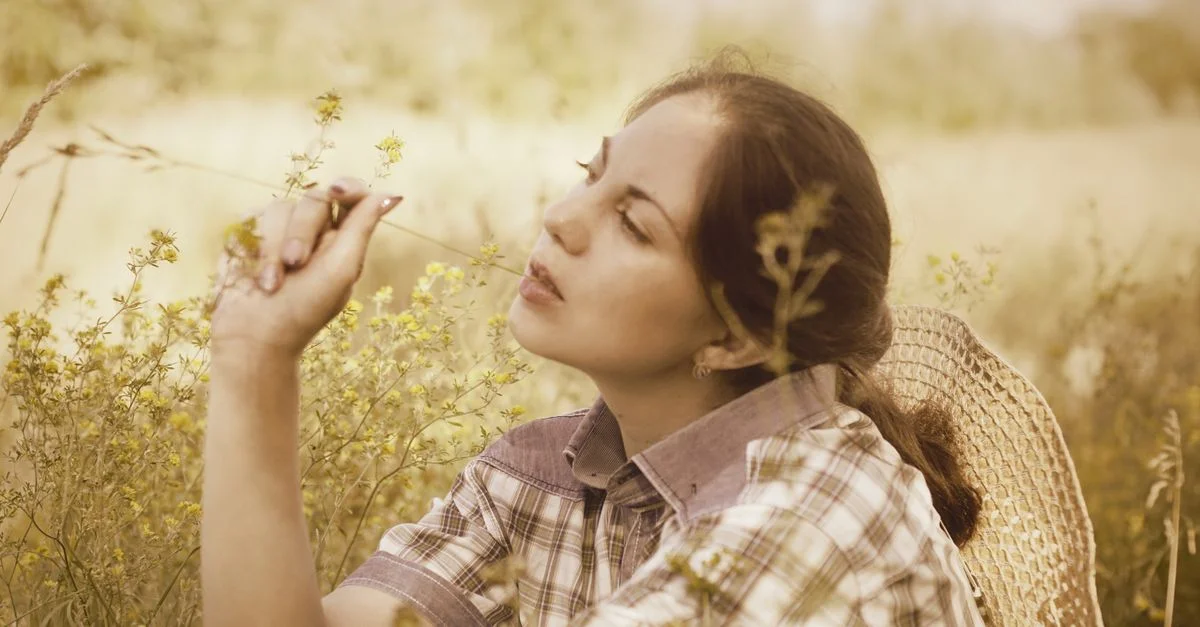 Une femme portant un chapeau en paille est assise paisiblement dans un champ, profitant de la beauté de la nature.