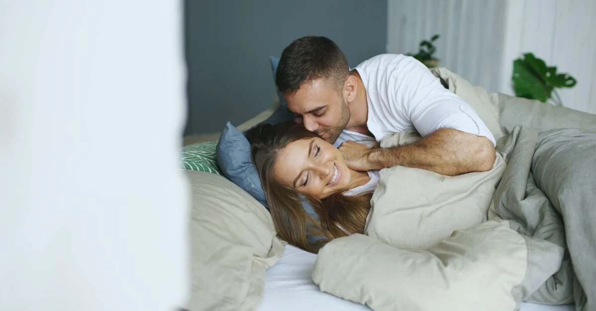 Couple romantique se blottissant au lit, évoquant chaleur et intimité avec un éclairage doux.