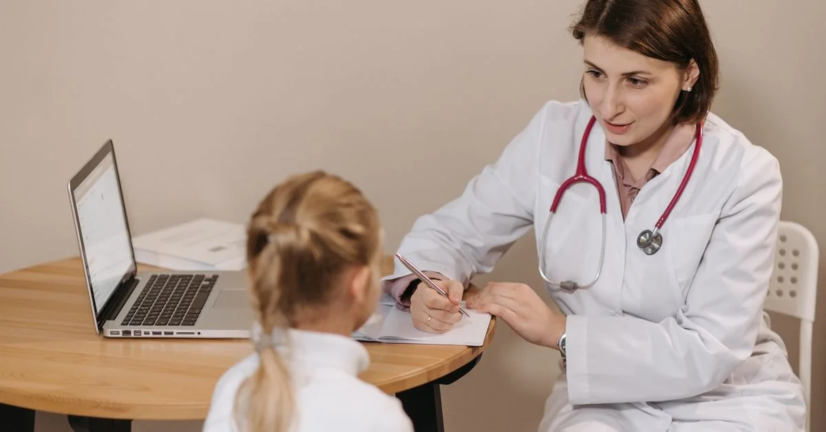Une médecin écoute attentivement une jeune fille lors d'une consultation médicale dans un cadre de bureau.