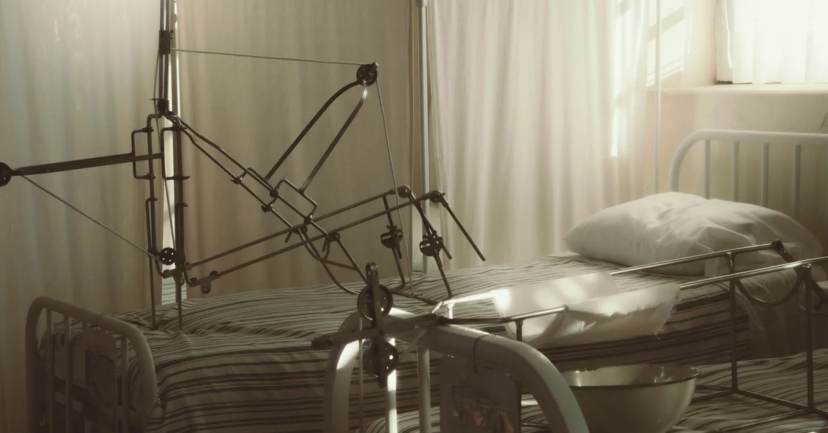 Un lit d'hôpital vide entouré d'équipements médicaux dans une pièce calme et ensoleillée.