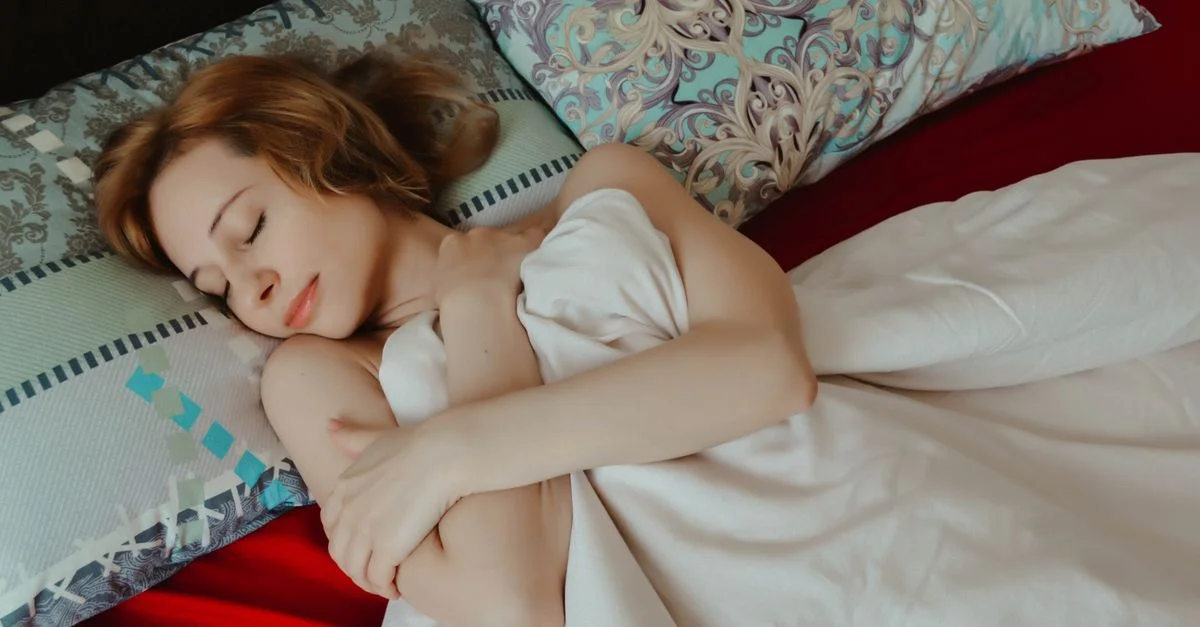 Une femme sereine dormant confortablement sous une couverture dans une ambiance de chambre chaleureuse.