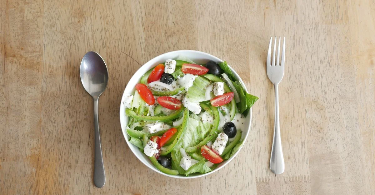 Une salade de légumes frais avec du fromage feta, des olives, des tomates cerises et une vinaigrette, placée sur une table en bois.