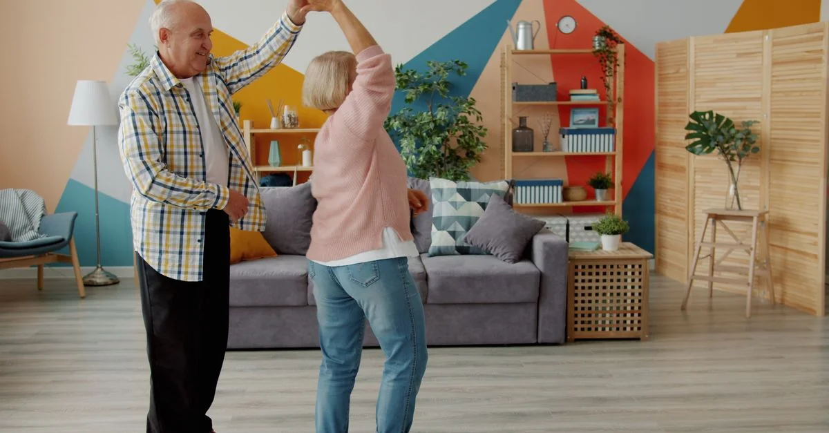 Un couple de seniors heureux danse dans un salon moderne, profitant de la vie.