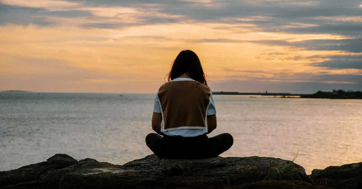 Une scène sereine d'une femme assise sur des rochers au bord de la mer pendant un coucher de soleil vibrant.