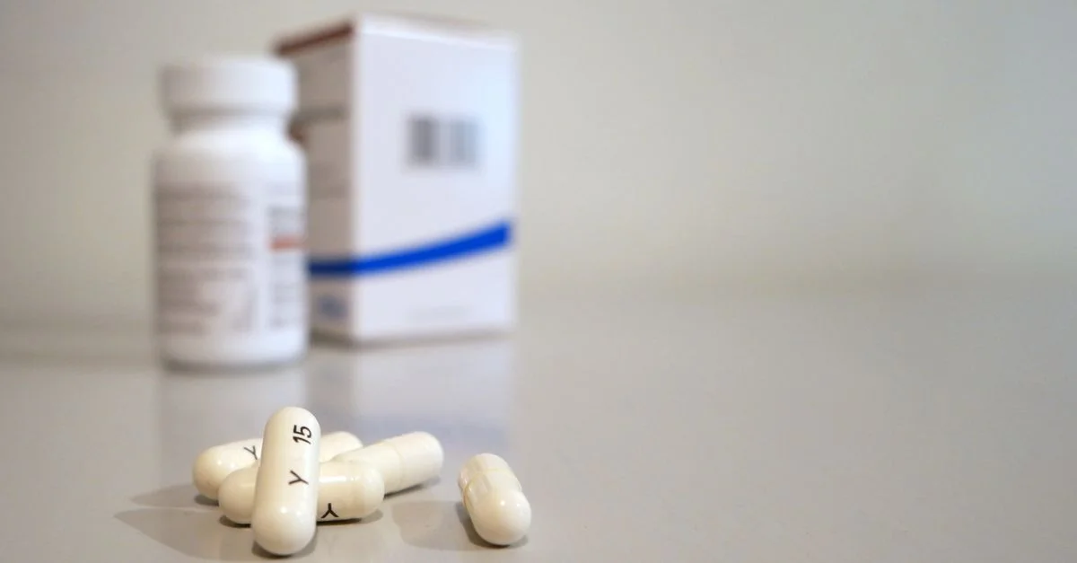 Gros plan sur des capsules blanches avec une bouteille de médicament et une boîte en arrière-plan.