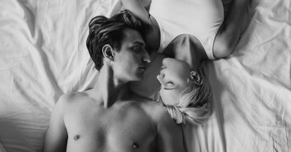 Photo intime en noir et blanc d'un jeune couple allongé ensemble sur un lit, exprimant la proximité et la romance.