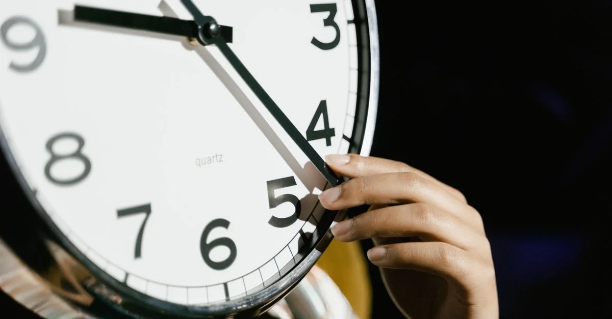 Une main ajustant l'heure sur une grande horloge analogique avec de grands chiffres.