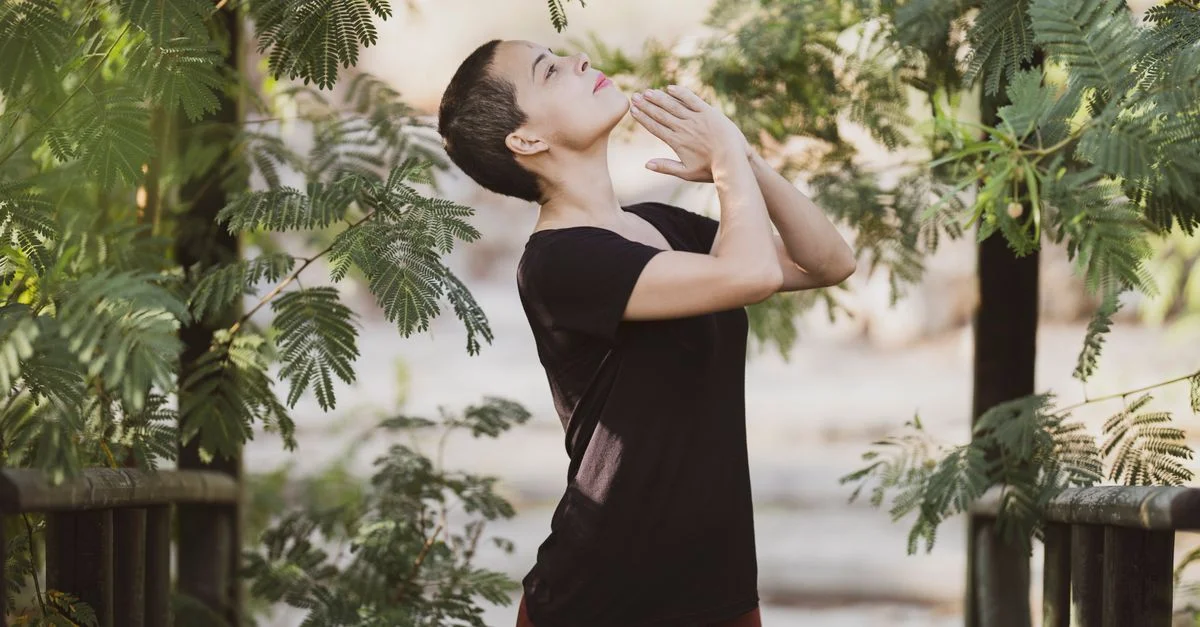 Une femme pratique la méditation entourée d'un feuillage vert luxuriant, profitant d'un moment paisible en plein air.