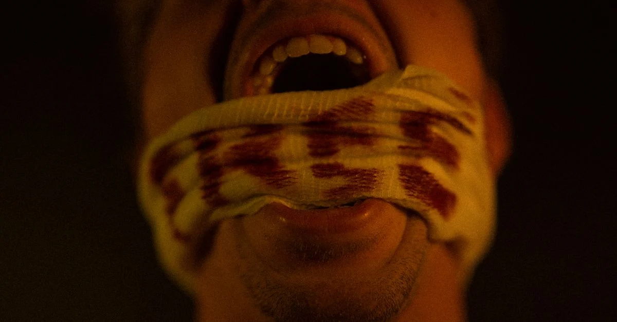 Portrait en gros plan d'un homme criant avec un bandage ensanglanté couvrant sa bouche, exprimant douleur et angoisse.