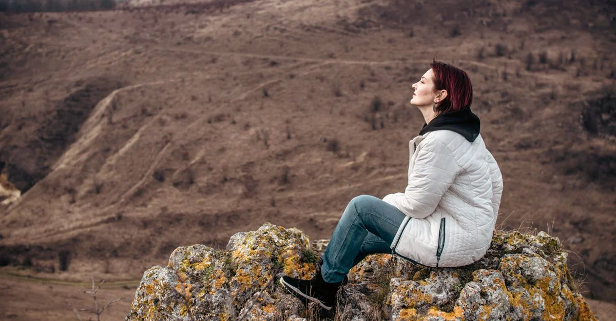 Femme profitant de la solitude au sommet d'une montagne rocheuse, les yeux fermés dans la détente.