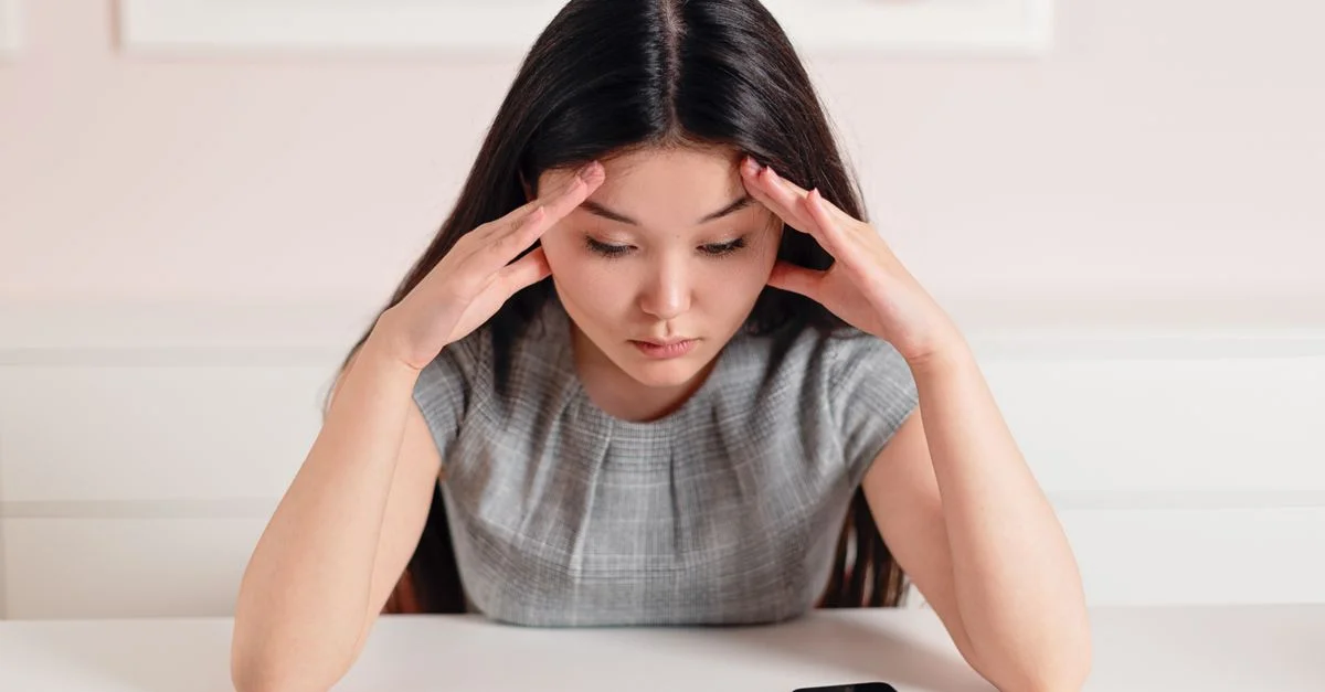 Femme d'affaires asiatique avec un mal de tête à son bureau, affichant stress et anxiété.