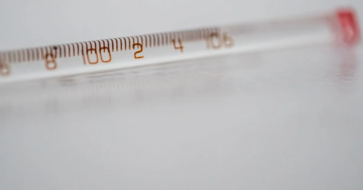 Gros plan détaillé d'un thermomètre en verre à mercure sur une surface blanche, montrant les mesures de température.