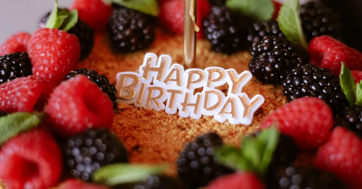 Gros plan sur un gâteau d'anniversaire garni de framboises et de mûres fraîches, avec une pancarte « Joyeux anniversaire ».