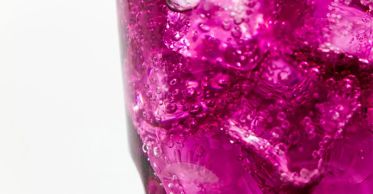 Une boisson violette rafraîchissante et vibrante avec des cubes de glace et des bulles dans un verre en gros plan.