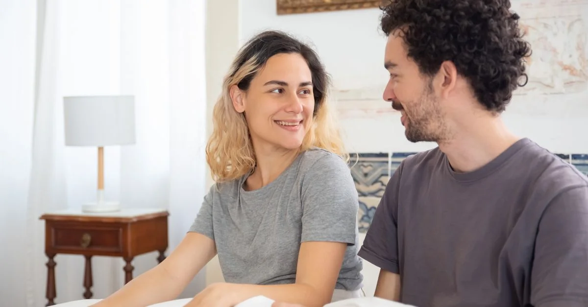 Couple souriant assis sur le lit dans une chambre lumineuse avec une décoration élégante.
