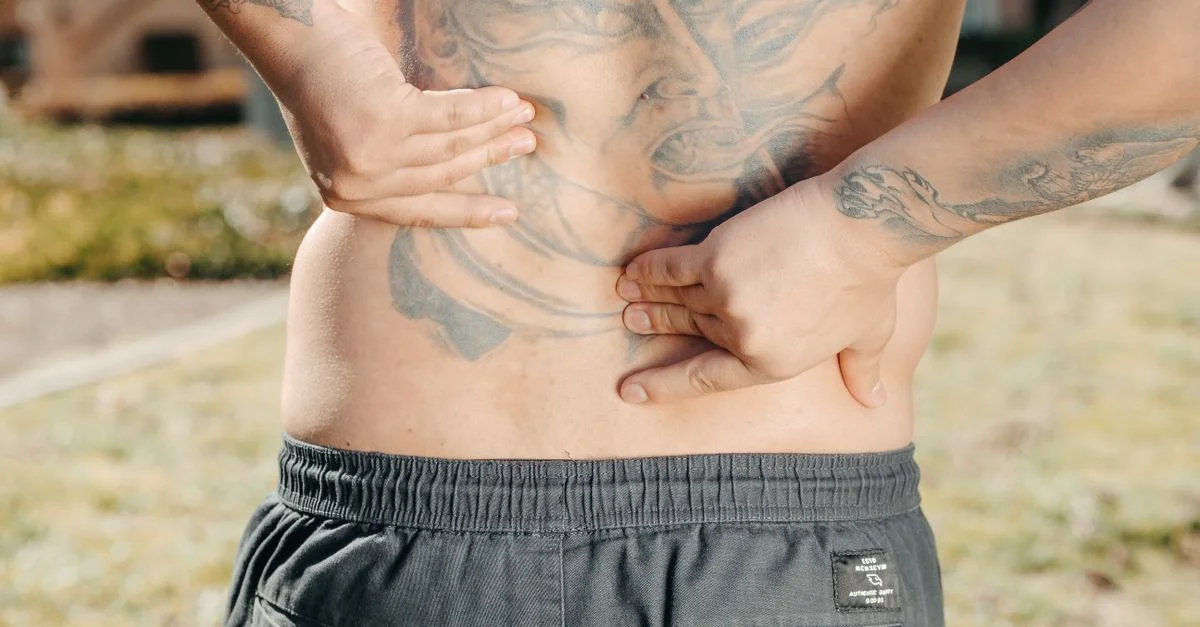 Gros plan d'un homme tenant son dos tatoué à l'extérieur, ressentant peut-être des douleurs dorsales.