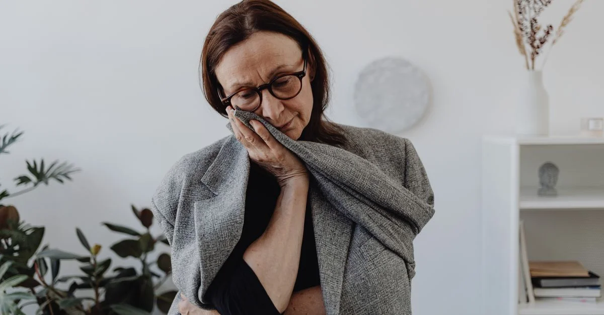 Une femme exprimant de la tristesse dans un cadre intérieur calme, entourée de plantes.