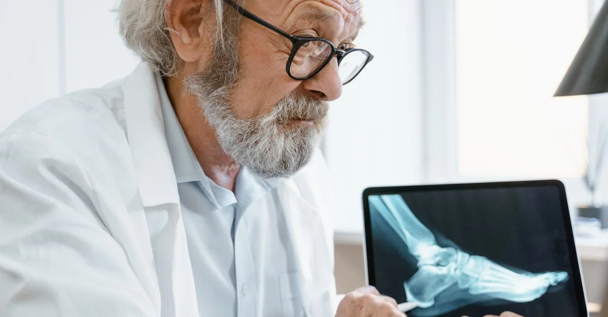 Médecin âgé en blouse blanche discutant des résultats de radiographie sur une tablette lors d'une consultation vidéo.