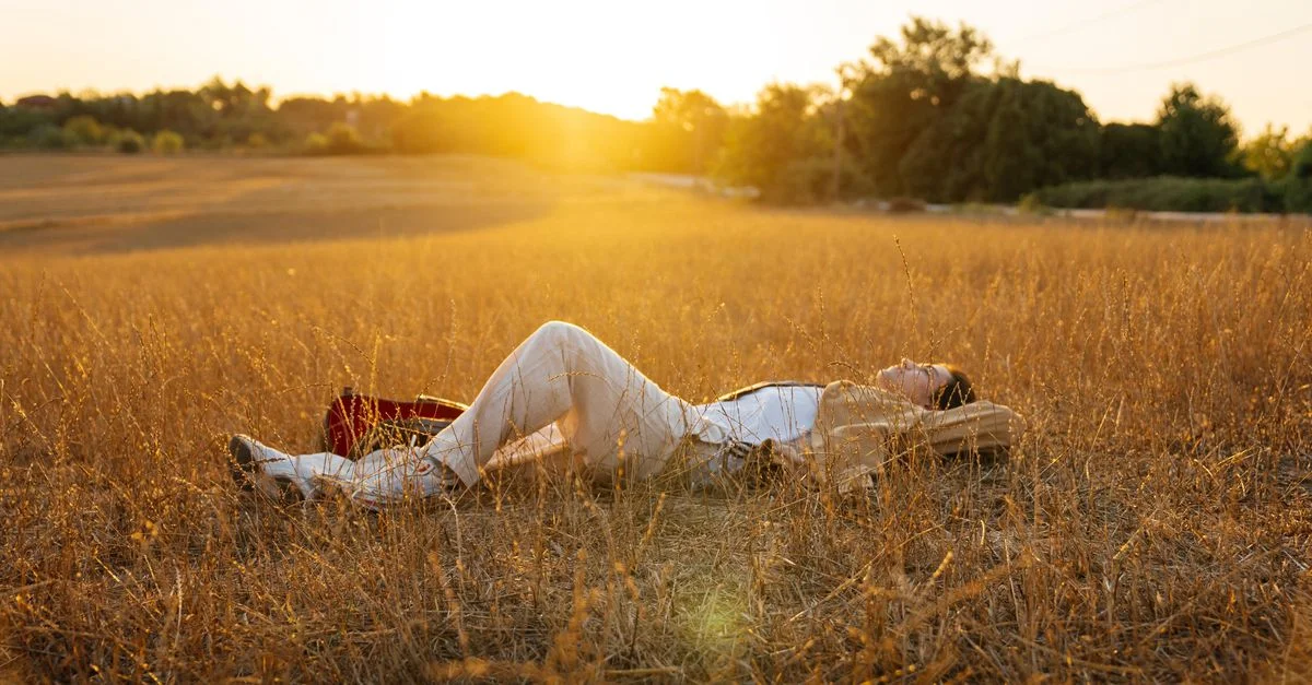 Une femme profite d'un moment serein allongée dans un champ ensoleillé au coucher du soleil.