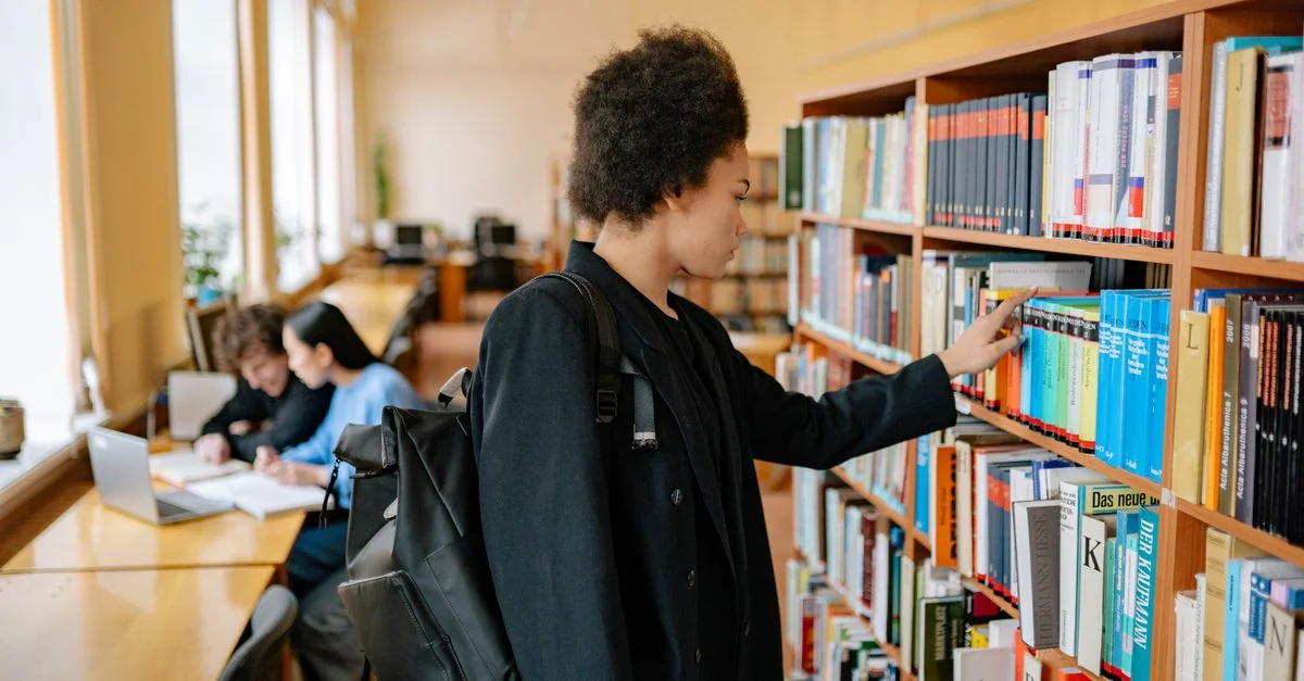 Étudiante concentrée avec un sac à dos choisissant un livre dans une bibliothèque universitaire.