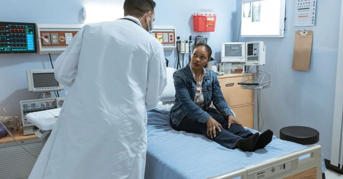 Un médecin consulte un patient dans une chambre d'établissement médical, entouré d'équipements de santé.