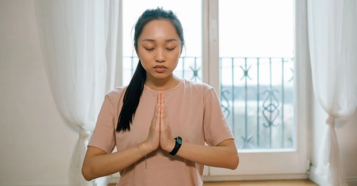 Femme asiatique pratiquant la méditation à l'intérieur, les mains ensemble, promouvant la paix et un mode de vie sain.