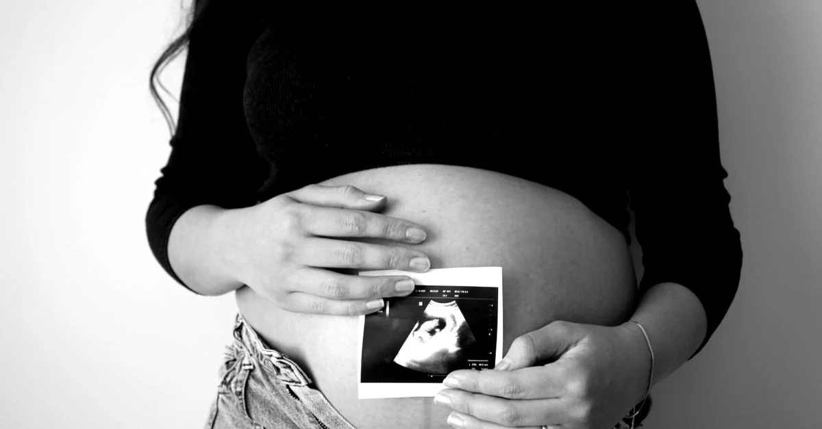 Une femme enceinte tient une photo d'échographie contre son ventre, symbolisant l'attente d'une maternité.