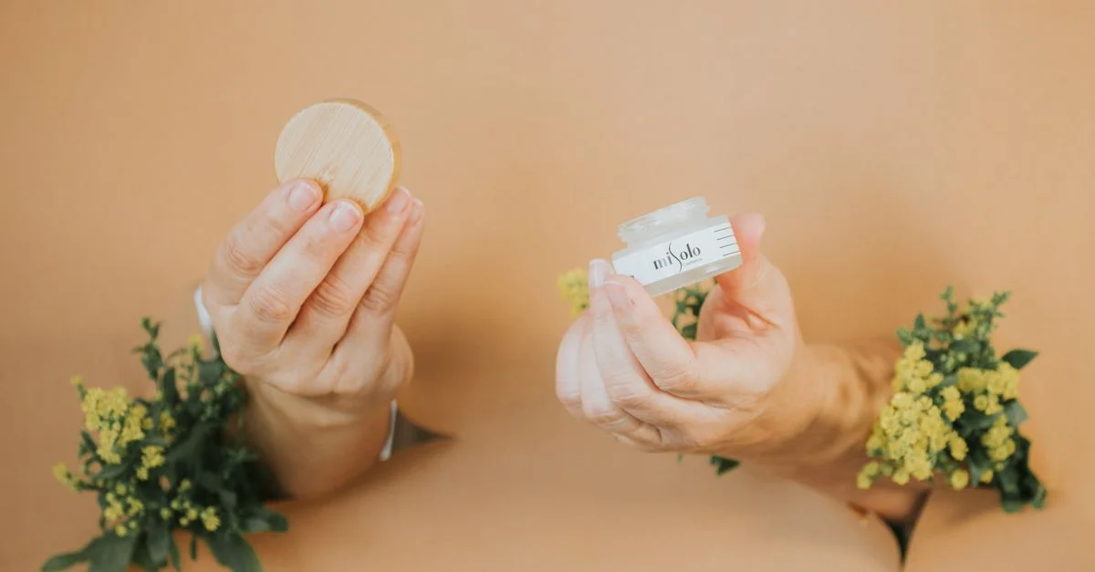 Mains tenant un pot de crème pour le visage naturel et son couvercle, entourées de fleurs.