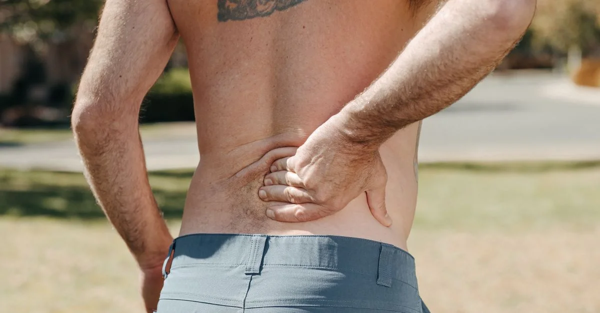Homme torse nu se tenant le bas du dos en extérieur, indiquant douleur ou inconfort.
