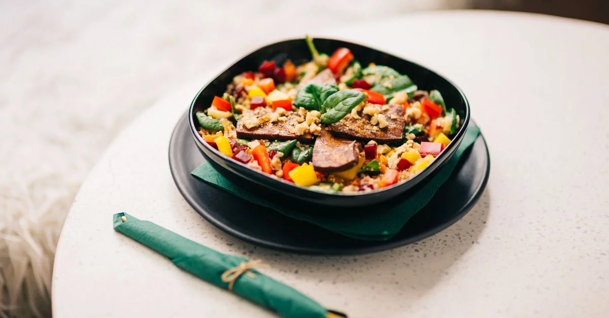 Bol de légumes colorés avec du tofu sur une assiette noire, parfait pour un mode de vie sain.