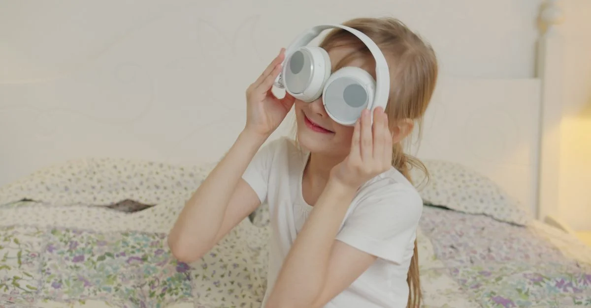 Un enfant heureux joue avec des écouteurs, faisant semblant que ce sont des lunettes de protection. Un moment de plaisir à l'intérieur.