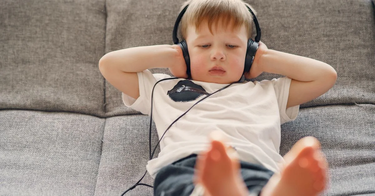 Un enfant est confortablement couché sur le canapé, écoutant de la musique avec des écouteurs dans un salon cosy.