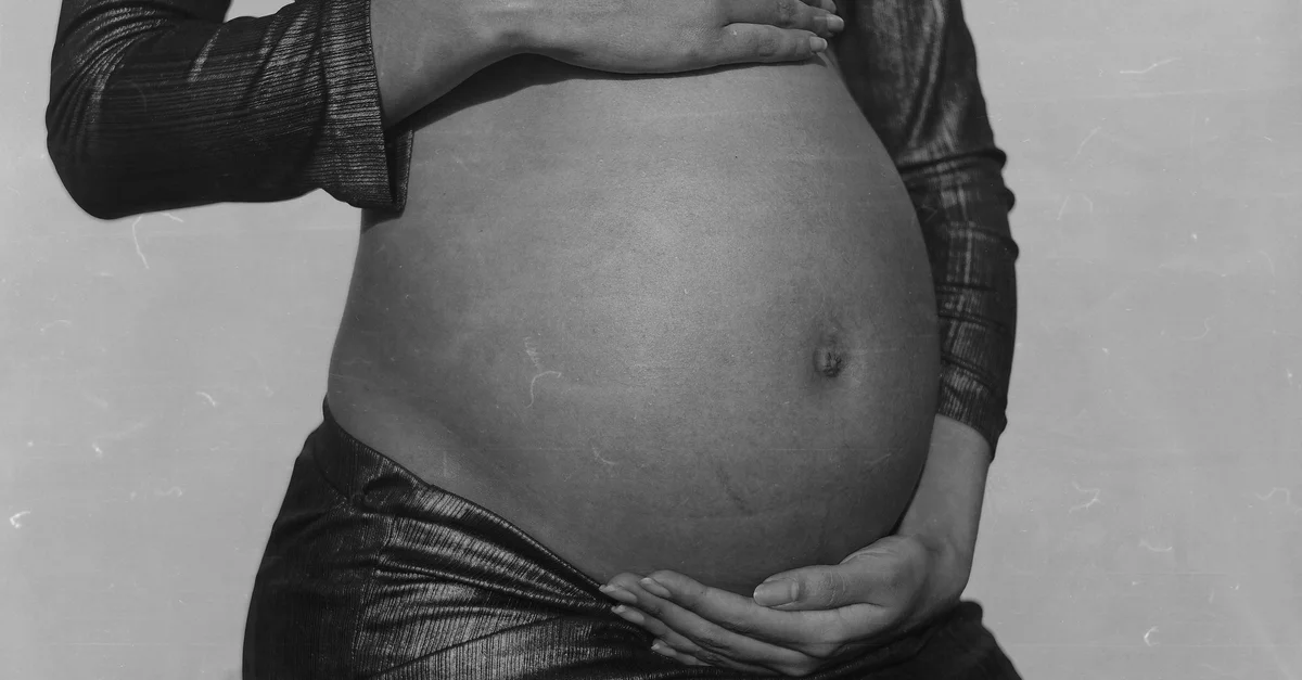 Gros plan en noir et blanc d'une femme enceinte étreignant tendrement son ventre à São Paulo.