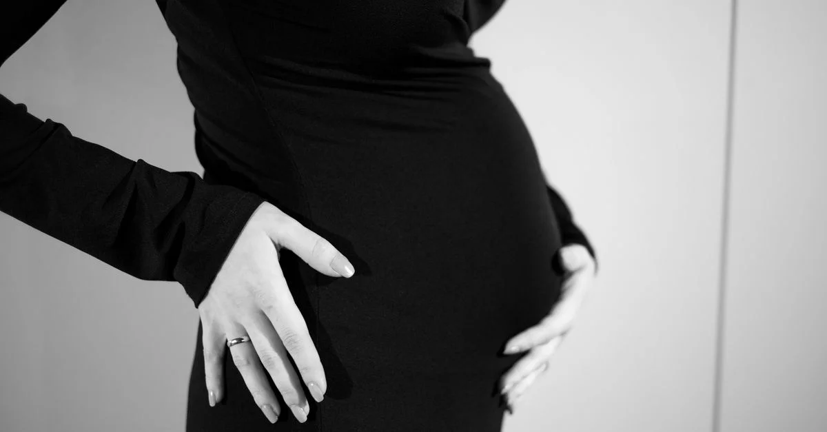 Vue latérale d'une femme enceinte tenant délicatement son ventre dans une robe noire.
