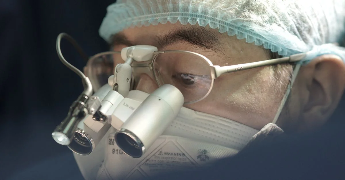 Chirurgien concentré portant un masque chirurgical et des loupes lors d'une opération.