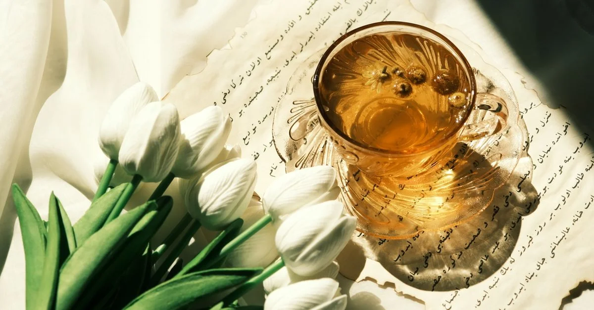 Tasse en verre de tisane et tulipes blanches sur papier avec écriture calligraphiée, créant une esthétique sereine.