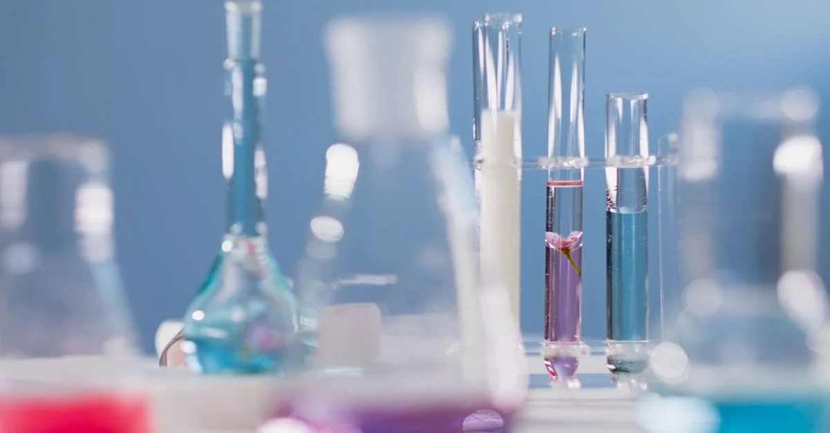 Gros plan sur divers instruments en verre avec des liquides colorés dans un environnement de laboratoire.