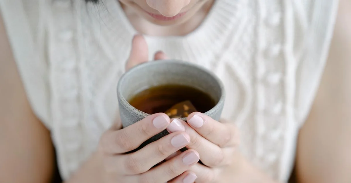 Une femme tient délicatement une tasse en céramique de tisane, appréciant l'arôme à l'intérieur.