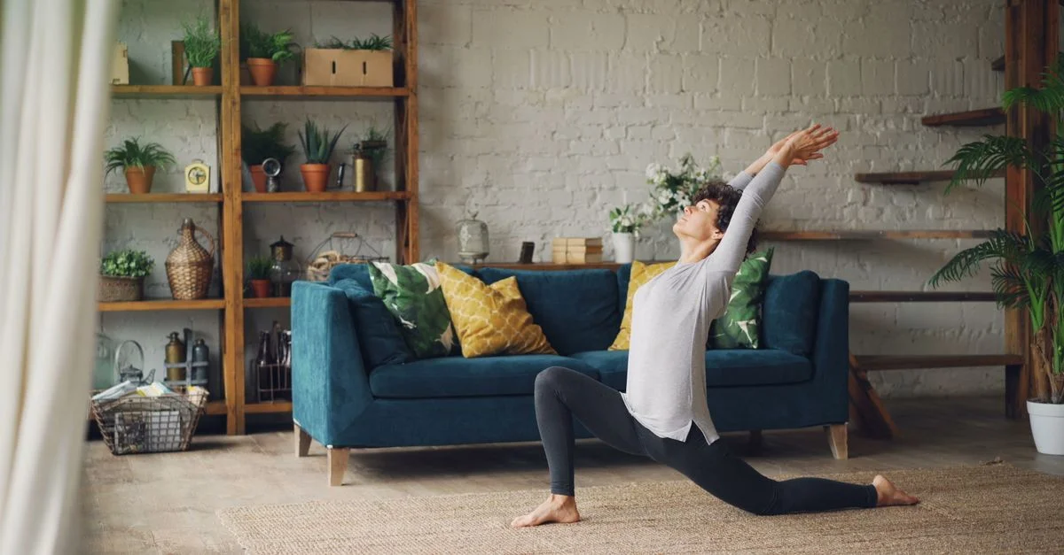 Femme effectuant du yoga dans un salon douillet avec des plantes et de la décoration, mettant en avant un mode de vie serein.