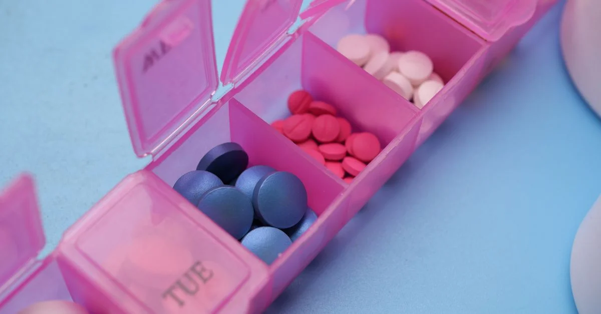 Organisateur de pilules rose avec des comprimés colorés disposés pour la gestion hebdomadaire des médicaments.