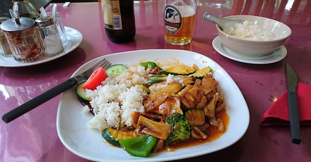 Plat asiatique savoureux de porc avec des légumes et du riz, servi avec une bière froide dans un restaurant chaleureux.