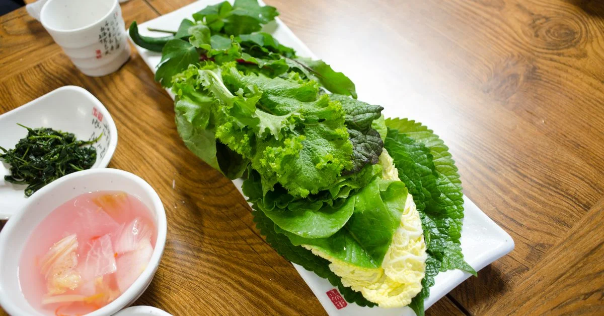 Plateau de légumes frais à feuilles sur une table en bois, prêt pour un repas sain.