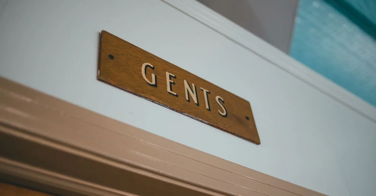 Vue en gros plan d'un panneau en bois rustique indiquant les toilettes 'Hommes' à l'intérieur.