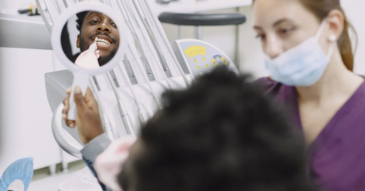 Un homme examine ses dents dans un miroir lors d'un contrôle dentaire. Un dentiste est présent.