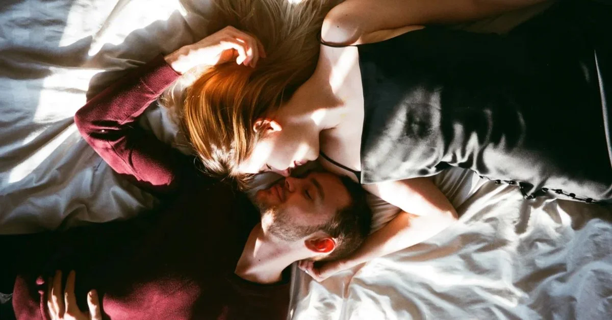 Un moment tendre capturé d'en haut, montrant un couple dans une étreinte intime sur un lit, baigné de lumière du soleil.