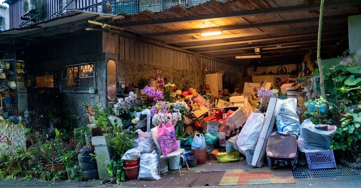 Un garage rempli de divers objets ménagers, de plantes et de désordre débordant sur la rue.